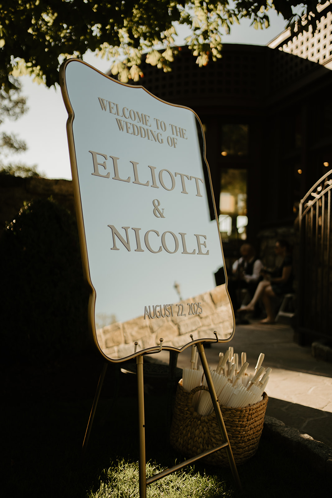 Elegant gold-framed mirror welcome sign for Elliott and Nicole's wedding standing on an easel outdoors.